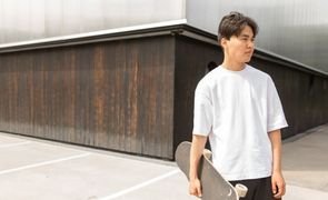 homem de camisa oversized branca com skate na mao